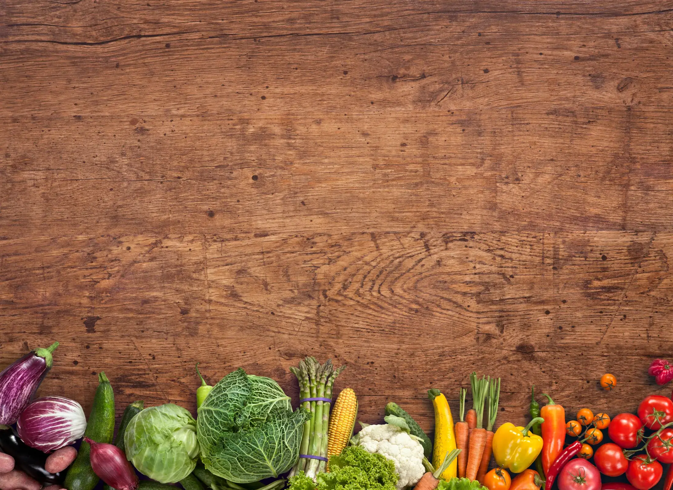 Fresh vegetables arranged along the edge of a dark timber table